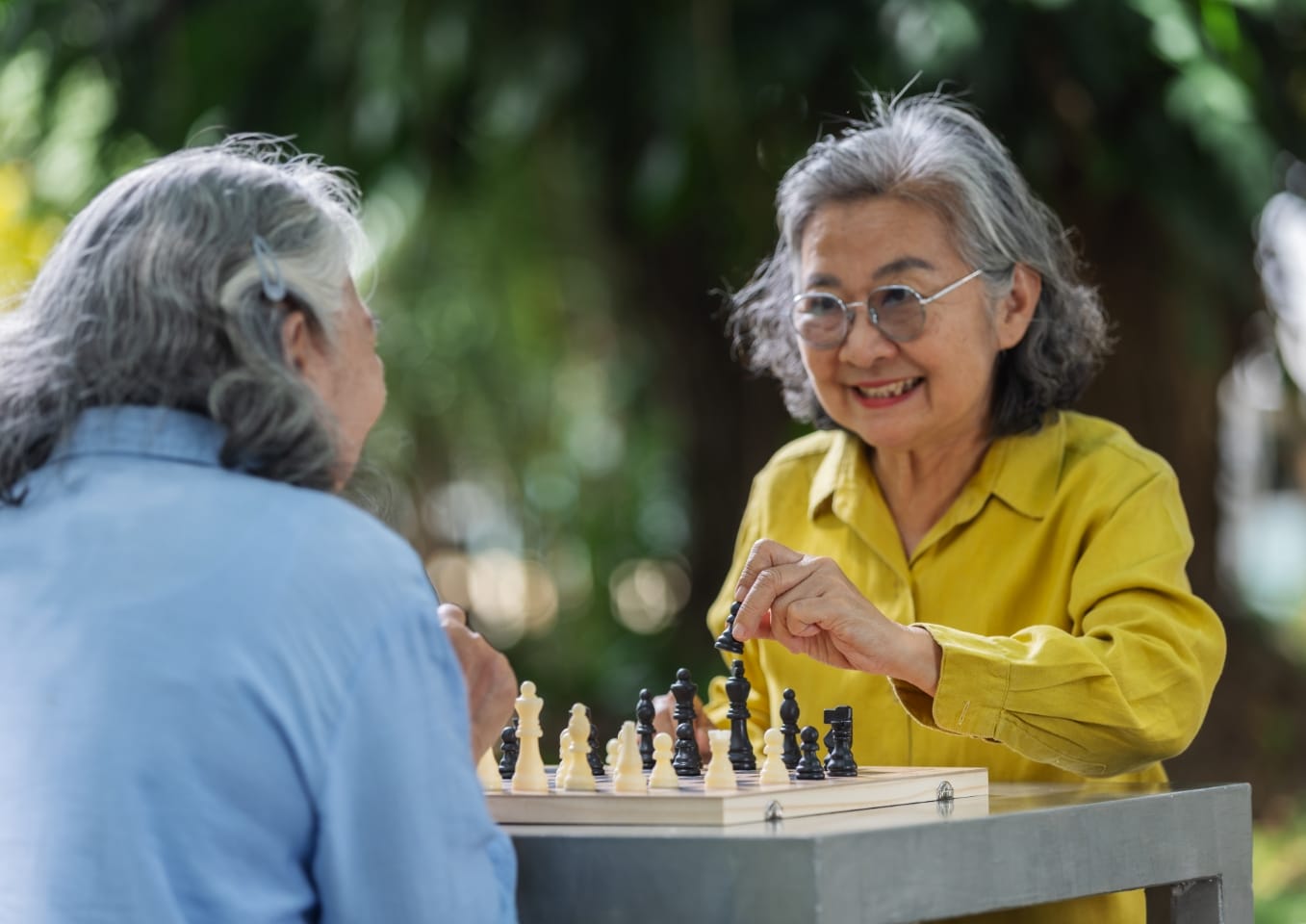 Two senior women enjoy a friendly chess match outdoors
